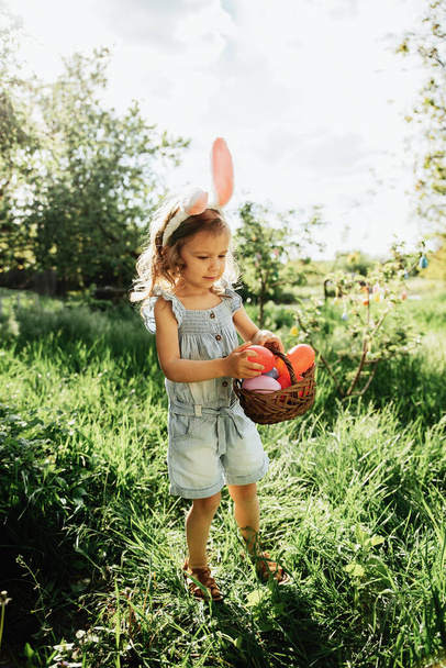 Baby with basket full of colorful eggs. Easter egg hunt. - Foto, imagen