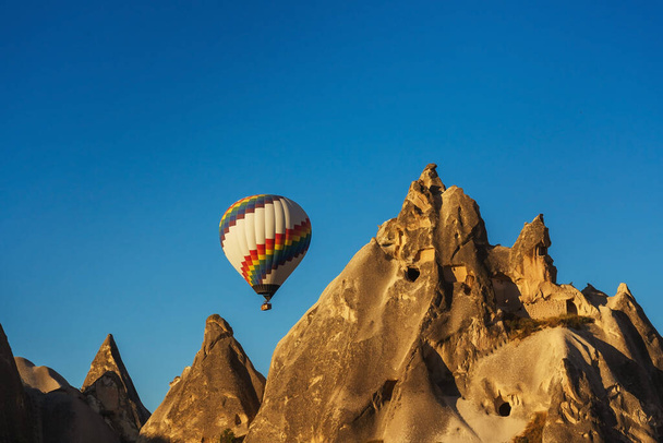Balloons over tuff houses in a valley in Cappadocia.Balloons in the sky in Cappadocia in Turkey. Flying colorful multicolored balloons in the sky - Fotó, kép