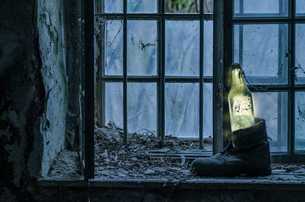 luminous bottle in a old shoe standing on the windowsill from a abandoned house - Photo, Image