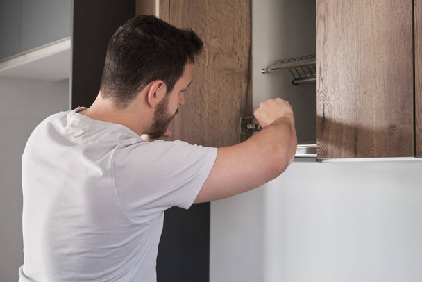 Giovane uomo latino che installa armadio in cucina utilizzando un cacciavite. - Foto, immagini