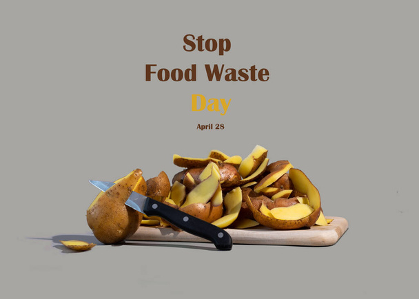 Έννοια της ημέρας διακοπής της σπατάλης τροφίμων. Οι φλούδες πατάτας είναι ένα από τα πιο συχνά πεταμένα αντικείμενα κατά την προετοιμασία του φαγητού. Γκρι φόντο. - Φωτογραφία, εικόνα