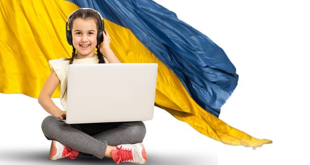 дівчинка дивиться домашній ноутбук. на фоні українського прапора - Фото, зображення