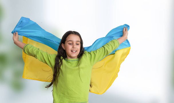 Child carries fluttering blue and yellow flag of Ukraine isolated on white. Ukraines Independence Day. Flag Day. Constitution day. Girl in traditional embroidery with flag of Ukraine - Фото, изображение