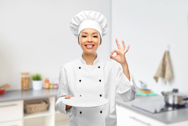 female chef holding empty plate and showing ok - Fotó, kép