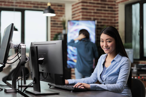 Χαμογελώντας 3D καλλιτέχνης και προγραμματιστής κάθεται στο γραφείο στο χώρο εργασίας γραφείο, ενώ εργάζονται σε νέο έργο παιχνίδι. - Φωτογραφία, εικόνα