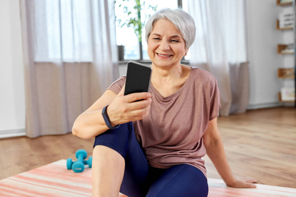 senior woman with smartphone exercising at home - Foto, afbeelding