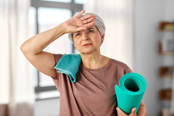 tired senior woman with yoga mat and towel - Foto, afbeelding