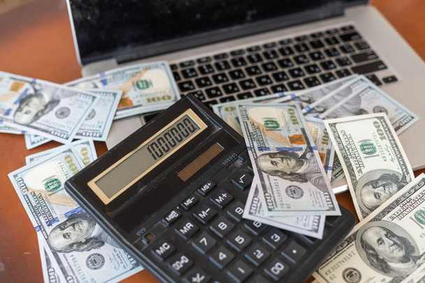 Finance concept: The United States hundred-dollar bills, calculator, bills, laptop on the table - Photo, image