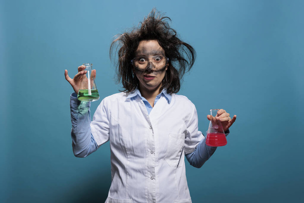 Bláznivý chemik drží Erlenmeyer sklenice naplněné neznámé chemické sloučeniny, zatímco na modrém pozadí. - Fotografie, Obrázek
