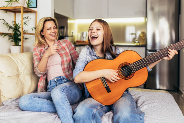Mother and daughter at home playing guitar and singing - Foto, imagen