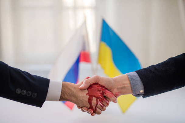 Representatives of Ukraine and Russia shaking hands, blood hand concept. - Фото, изображение