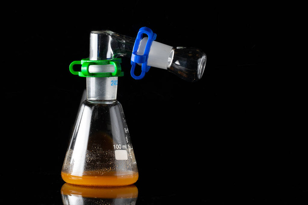 Transparent lab bottle cylinder with orange liquid inside isolated in black background for study research. - Foto, Imagen