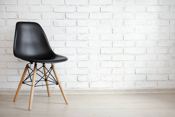 zwarte stoel over witte baksteen muur achtergrond met kopieerruimte - Foto, afbeelding