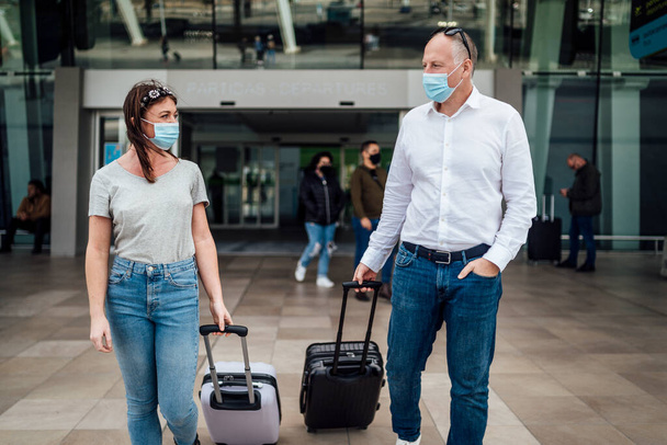 Un couple d'amis en masques de protection bavardant tout en quittant l'aéroport avec leurs bagages - Photo, image