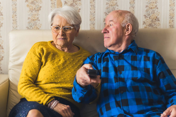 Ritratto di una coppia anziana che guarda la televisione seduta sul divano - l'uomo tiene il telecomando - Foto, immagini