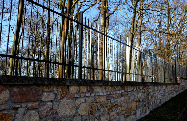 πύλη και φράχτη στο κάστρο στον φθινοπωρινό ήλιο. Το πλέγμα που τερματίζει το τέλος του τείχους προστάτευε τους κλέφτες από ανάρμοστους εισβολείς. σχήμα ακίδας με μεντεσέδες στάσεων και θυρών - Φωτογραφία, εικόνα