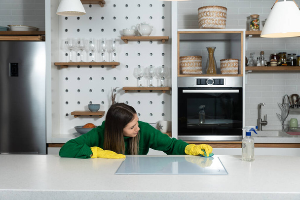 Young happy woman college university student clean the kitchen in her new rented apartment. Female with yellow cleaning rubber protective gloves on hands doing housework. - Фото, зображення