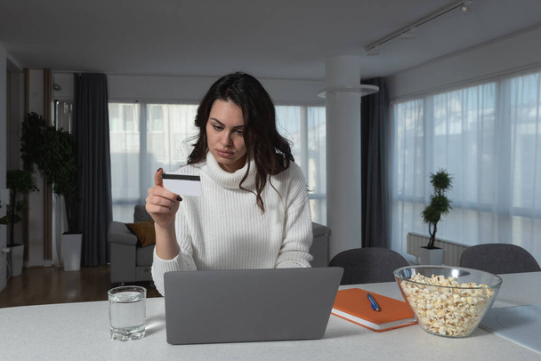 Young happy woman holding credit card and using laptop computer. Businesswoman working at home. Online shopping e-commerce internet banking spending money working from home concept - Photo, Image