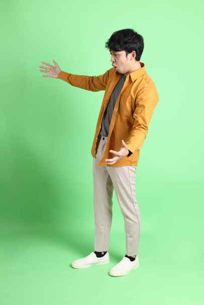 O jovem homem asiático adulto com roupas casuais inteligentes em pé no fundo verde claro. - Foto, Imagem