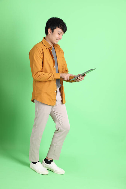 Le jeune homme asiatique adulte avec des vêtements décontractés intelligents debout sur le fond vert clair. - Photo, image