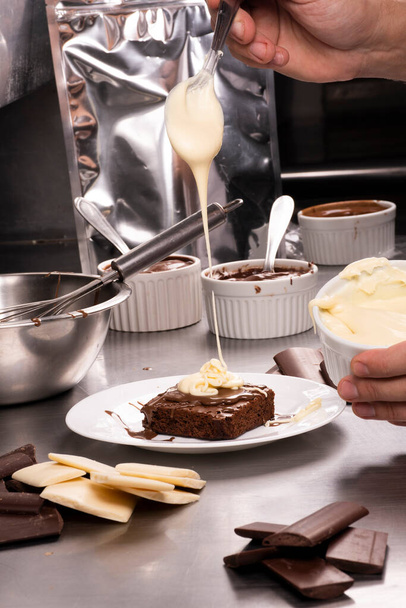 επαγγελματική παραγωγή γλυκών ρίχνοντας λιωμένη λευκή σοκολάτα σε brownie στη βιομηχανική κουζίνα - Φωτογραφία, εικόνα