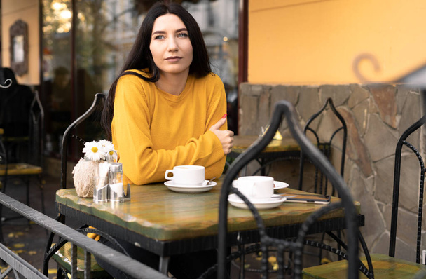Relaxation in autumn in a street cafe, brunette woman drinking coffee and daydreaming, lunch break, copy space - Foto, Imagen