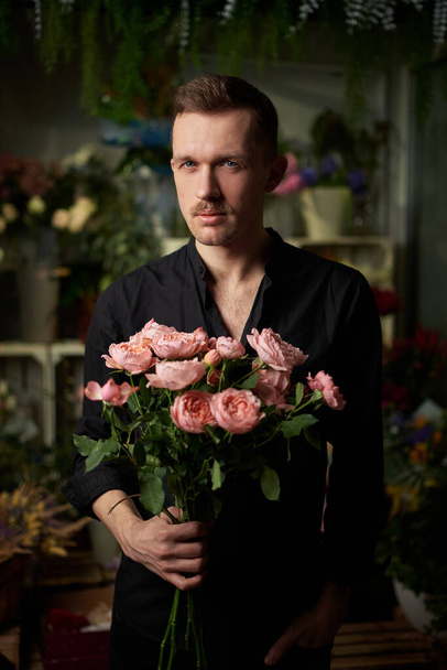 Елегантний чоловік мачо в чорній сорочці тримає букет з рожевих троянд
 - Фото, зображення