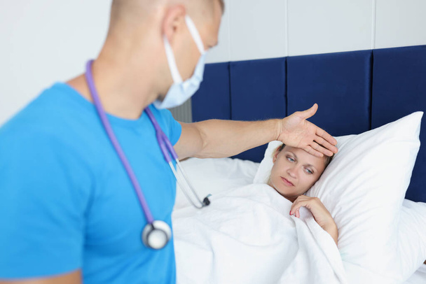 Doctor keeps hand on forehead of sick woman on bed - Valokuva, kuva