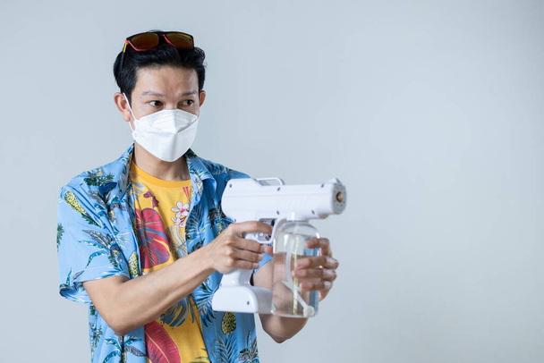 Asijský muž s lékařskou maskou drží zbraň na sprej dezinfekční, Songkran Festival v Thajsku, V covid-19 preventivní opatření, Kopírovat prostor. - Fotografie, Obrázek