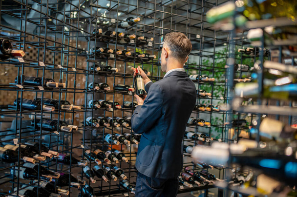Ein Mann sucht sich in einem Weinladen eine Flasche Wein aus - Foto, Bild