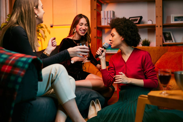 Een groep jonge multiraciale vrouwen die een meidenavond thuis hebben. Ze geven een feestje en zingen popliedjes op karaoke avond.. - Foto, afbeelding