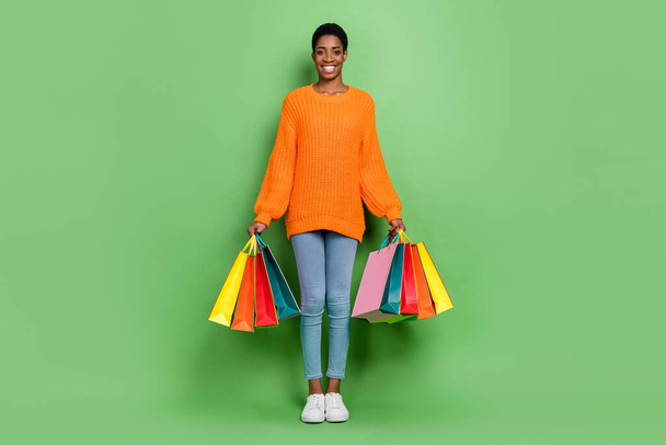 Full size photo of sweet millennial lady hold bags wear sweater jeans shoes isolated on green background - Photo, Image