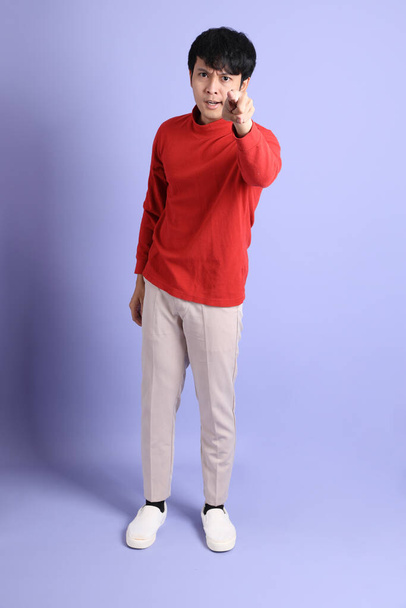 Nuori aikuinen Kaakkois-Aasian mies punainen pitkähihainen paita seisoo vaaleanvihreä tausta. - Valokuva, kuva