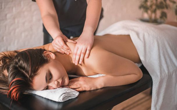 Body care. A masseur gives a young girl a massage, rests in an aesthetic spa, side view of the skin care concept. - Zdjęcie, obraz