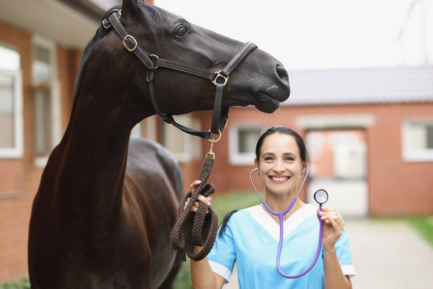 Glimlachende dierenarts met paard houdt stethoscoop close-up - Foto, afbeelding