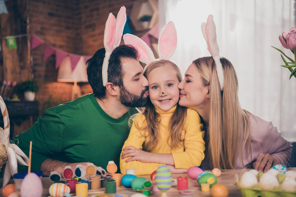 Portrait of attractive cheerful family preparing party drawing eggs kissing girl parenthood motherhood generation indoors - Foto, Bild