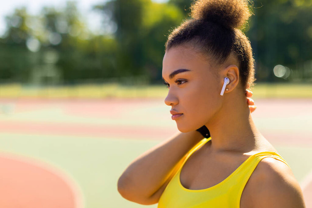 Sportieve zwarte vrouw in gele sportkleding luisteren naar muziek - Foto, afbeelding