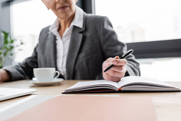 обрізаний вид розмитого економіста з ручкою, що сидить біля блокнота та чашки кави
 - Фото, зображення