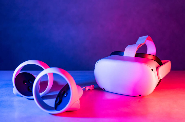VR Headset technologie pro zábavní zážitek. Brýle a ovladače virtuální reality na stole v neonovém osvětlovacím studiu. Metaverzní vizualizace a simulace, 3D, AR, VR, Inovace futuristiky. - Fotografie, Obrázek