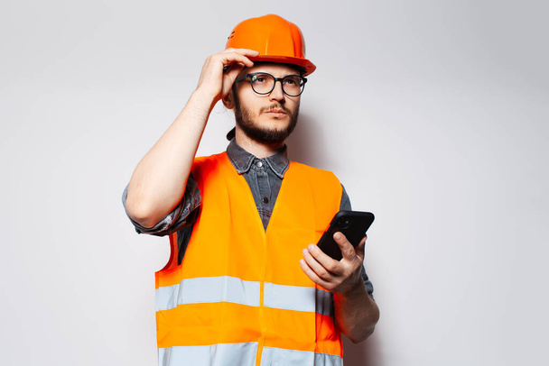 Mladý stavební pracovník s chytrým telefonem v ruce na bílém pozadí. - Fotografie, Obrázek