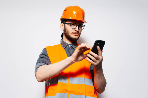 Portrét mladého stavebního dělníka psaní na smartphone na bílém pozadí. - Fotografie, Obrázek