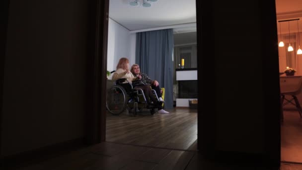 Νεαρός άντρας και γυναίκα σε αναπηρικό καροτσάκι κάθονται στο σαλόνι και μετά βγαίνουν έξω. - Πλάνα, βίντεο