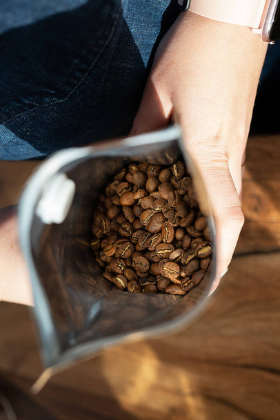 Ο καβουρδισμένος κόκκος καφέ συσκευάζεται σε μια τσάντα που ο barista κρατά στα χέρια του. Κάτοψη, έννοια παρασκευής καφέ - Φωτογραφία, εικόνα