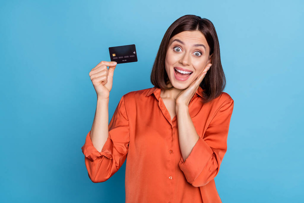 Portrait of attractive cheerful amazed girl holding in hand bank card nfc method great news isolated over bright blue color background - Valokuva, kuva