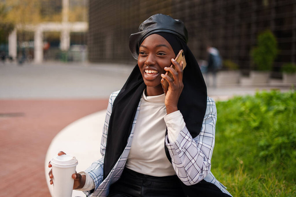 Femme noire joyeuse avec café à emporter parlant sur smartphone - Photo, image