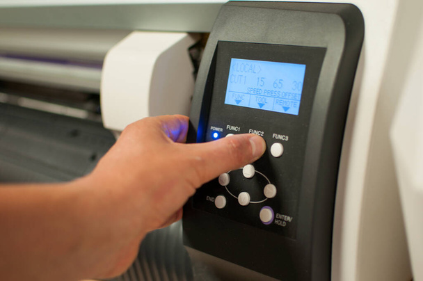 Ο χειριστής εκτυπωτή πατάει το κουμπί τροφοδοσίας στο μηχάνημα και αρχίζει την εκτύπωση. Ανδρικό χέρι και πίνακας με κουμπιά. - Φωτογραφία, εικόνα
