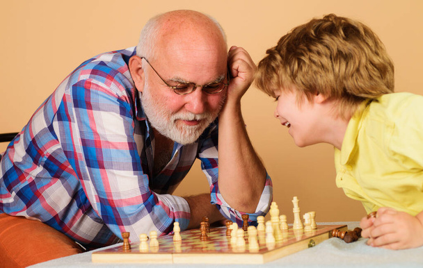 祖父は孫にチェスを教える。シニア男はチェスの試合で次の動きについて考えて. - 写真・画像