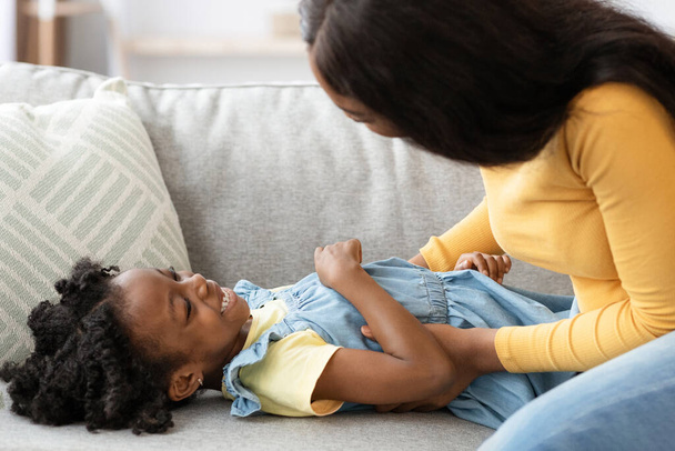 Vrolijke zwarte moeder hebben plezier met haar kleine dochter thuis - Foto, afbeelding
