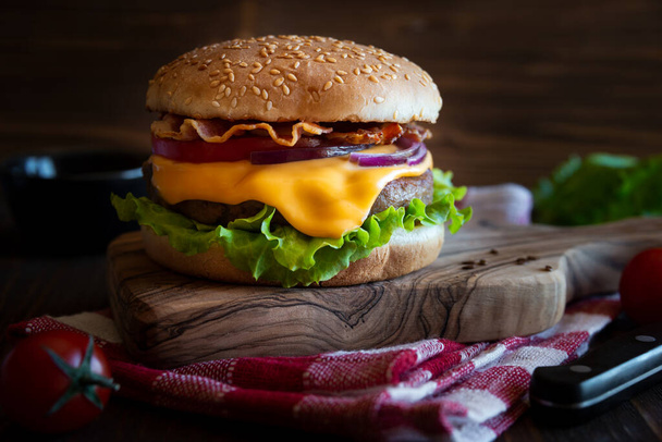 Hamburguesa con queso, tocino, tomate y lechuga sobre fondo de madera oscura
 - Foto, Imagen