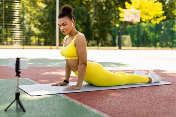 Young black woman stretching back on mat with cellphone - Photo, Image